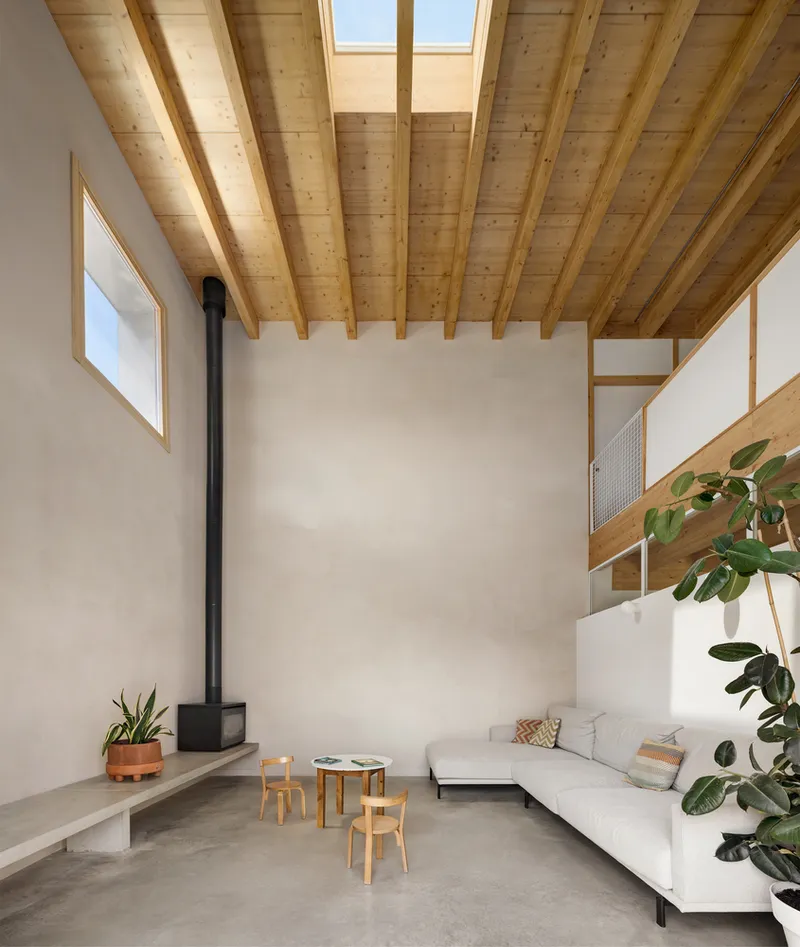 Double-height living room with exposed timber beams and decking ceiling under skylight above a black wood stove