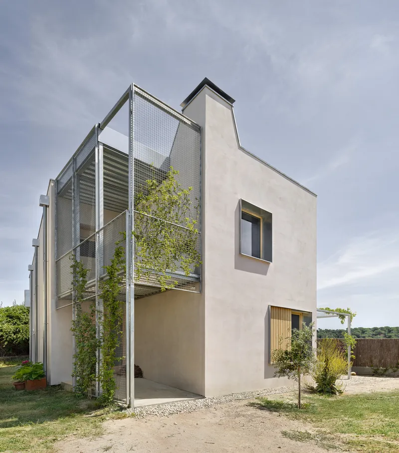 Rear facade showing perforated metal staircase enclosure with climbing vines beside a rendered tower volume under grey sky