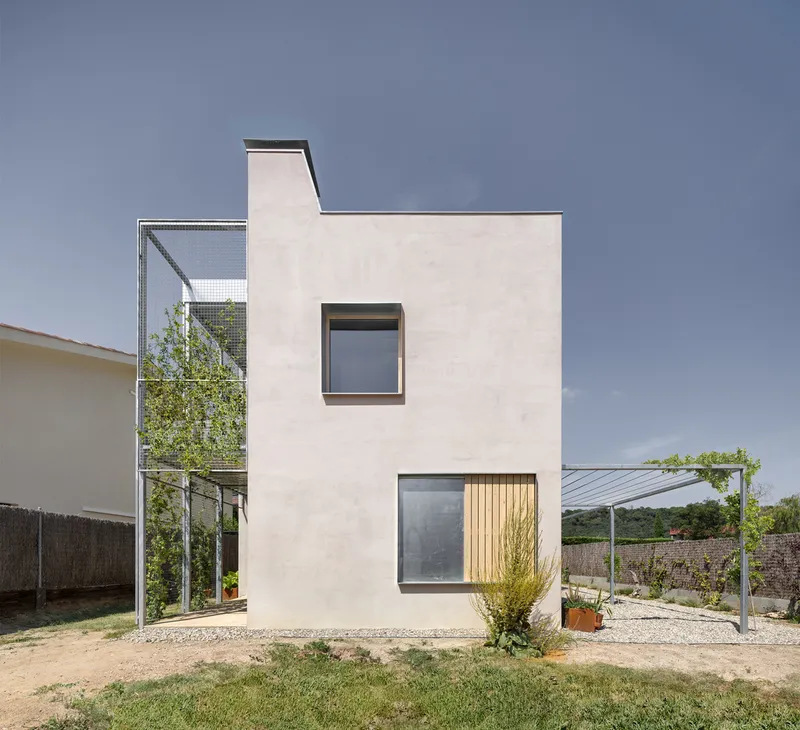 Street-facing elevation with stacked square windows on pale stucco wall and metal mesh stair tower with green climbers
