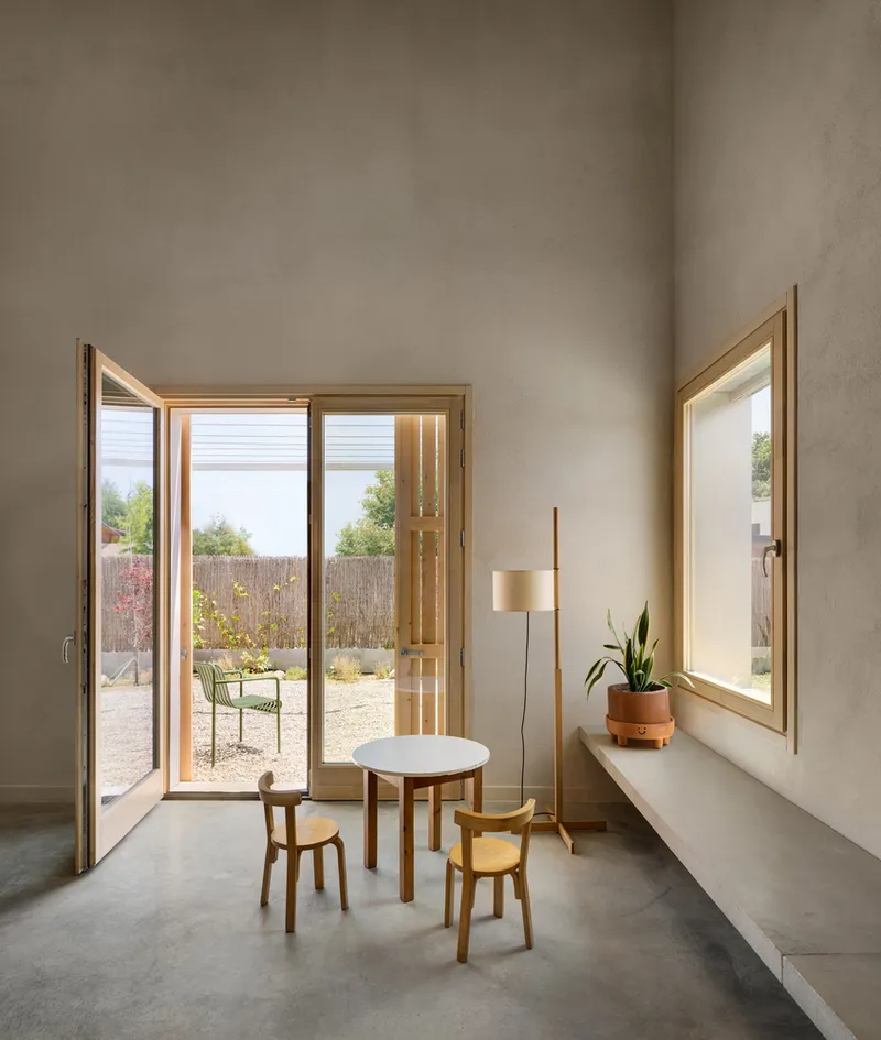 Glazed door opening to gravel courtyard with reed fence and a single round table with two stools