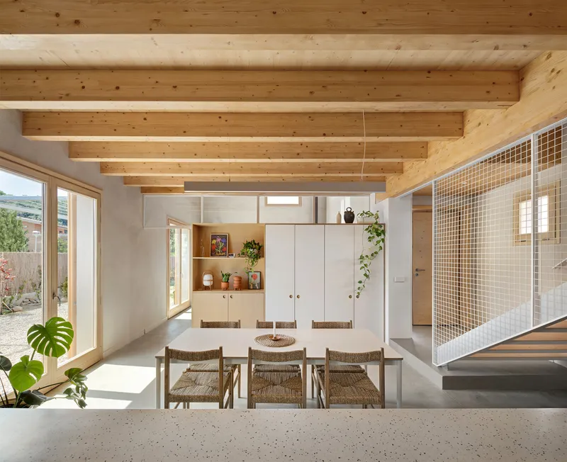 Open-plan dining space with exposed timber beams and mesh partition wall in daylight