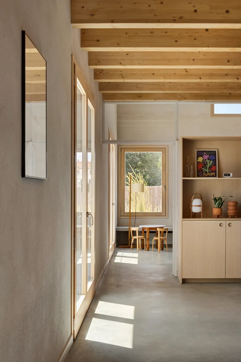 Sunlit hallway with concrete floor and timber-framed glazing casting shadows across the passage