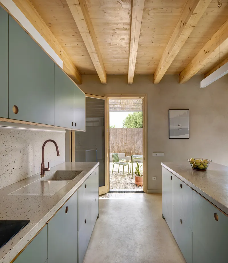 Galley kitchen with terrazzo countertops and timber-framed door opening to courtyard beyond