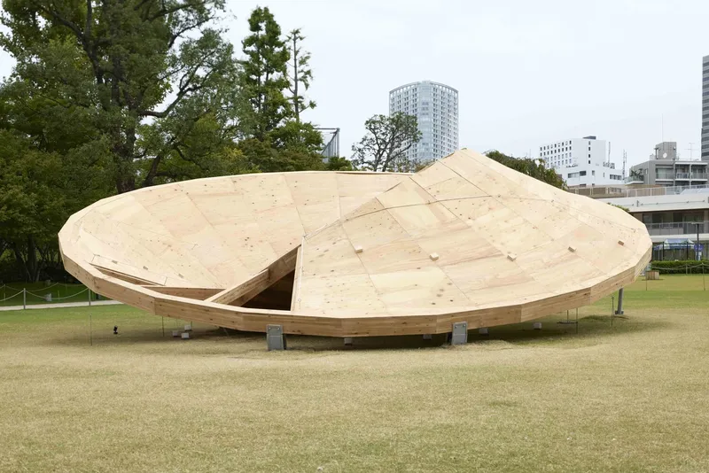 Side view of the curved plywood shell pavilion on steel supports in an open lawn