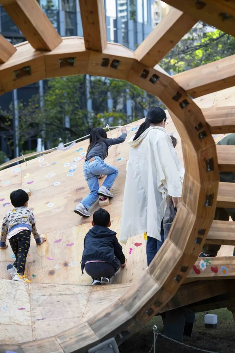 Children and adults climbing the sloped plywood deck surface with scattered flower petals