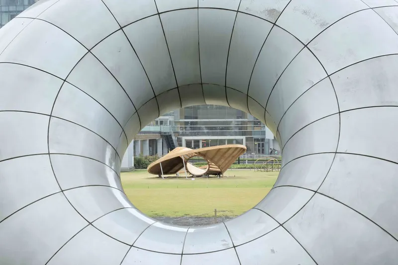 Through the circular metal portal framing the timber pavilion on the lawn beyond