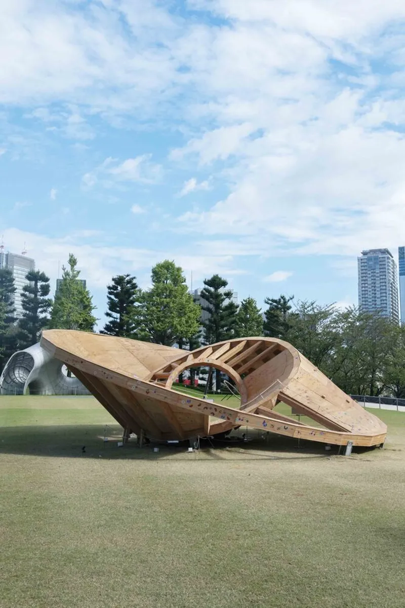 The laminated timber shell pavilion in the park under a partly cloudy sky