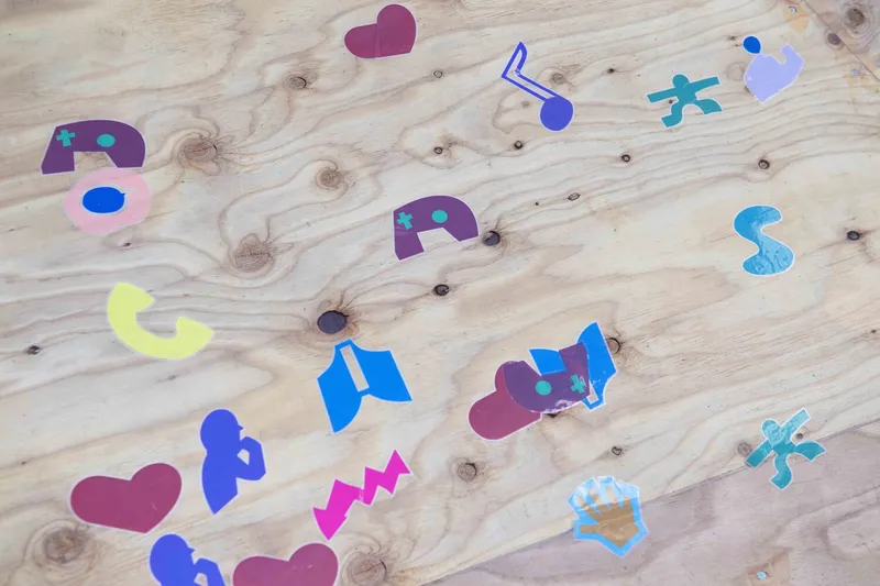 Colorful abstract graphic shapes scattered across a light plywood surface with visible knots and grain