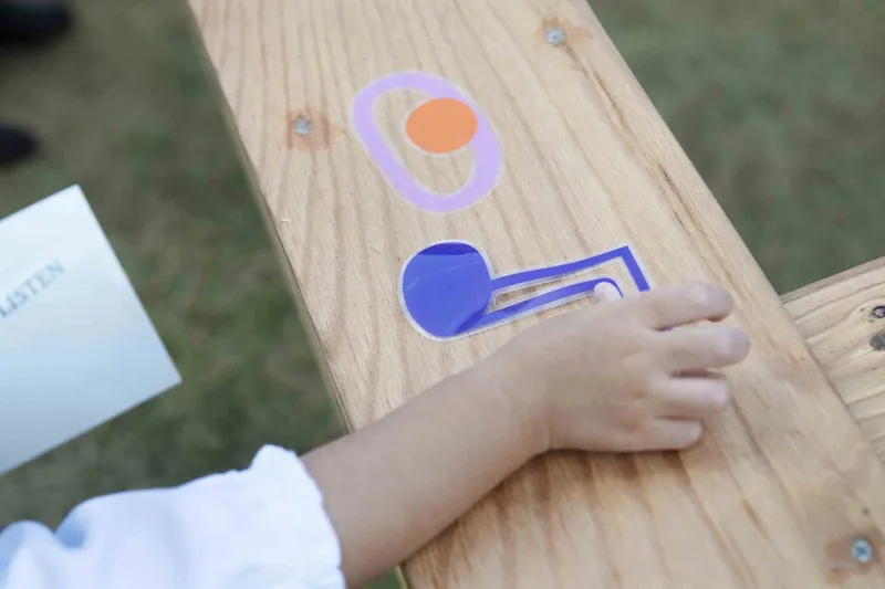 Child's hand reaching across a timber surface marked with graphic symbols in sunlight
