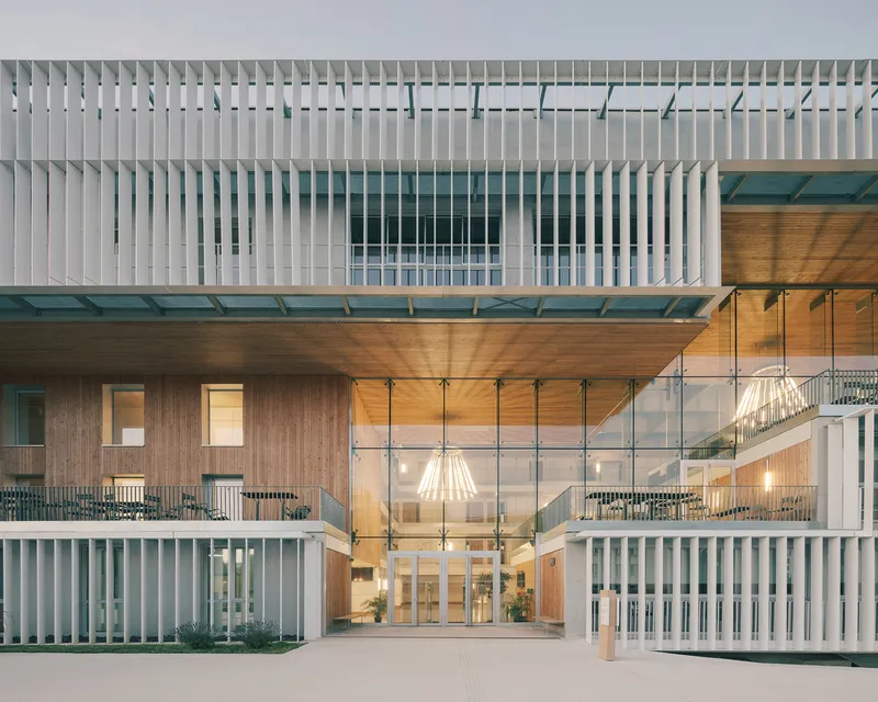Entry facade with vertical white louvers above a timber-lined canopy and glazed lobby at dusk