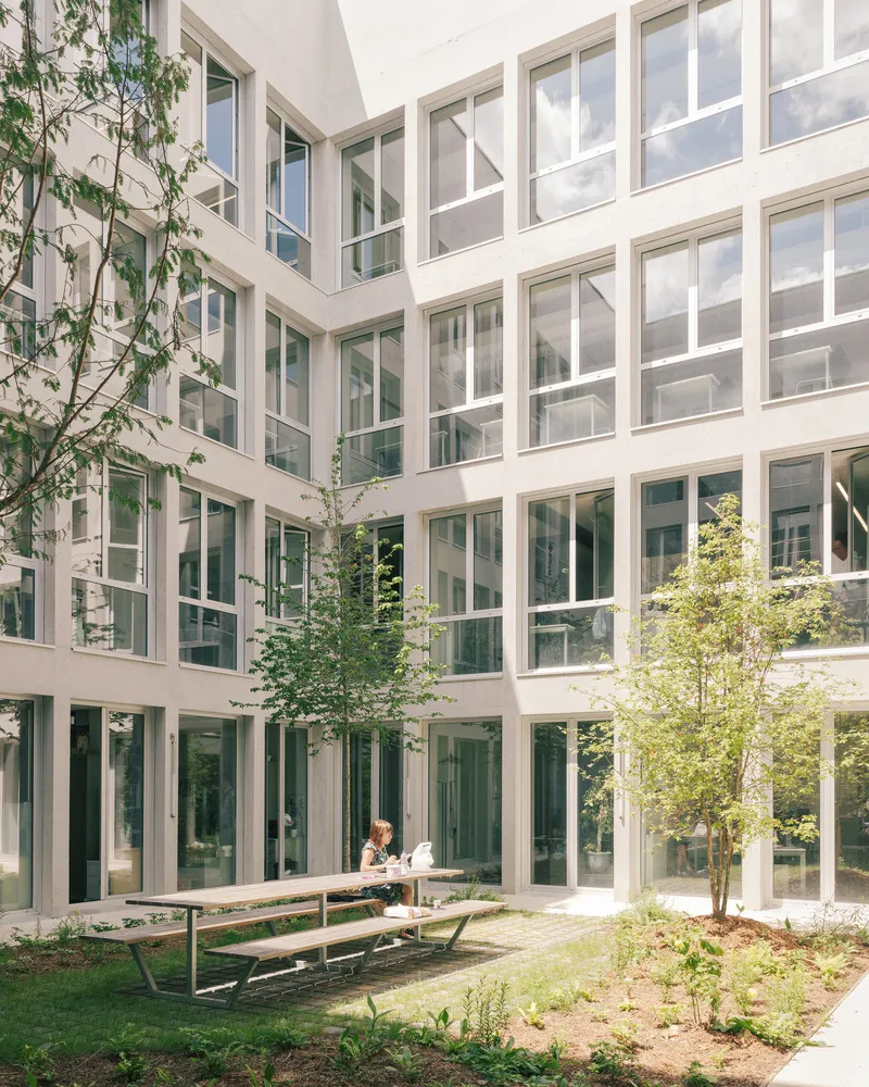 Interior courtyard with white-framed windows surrounding a grassy lawn, picnic table and young trees