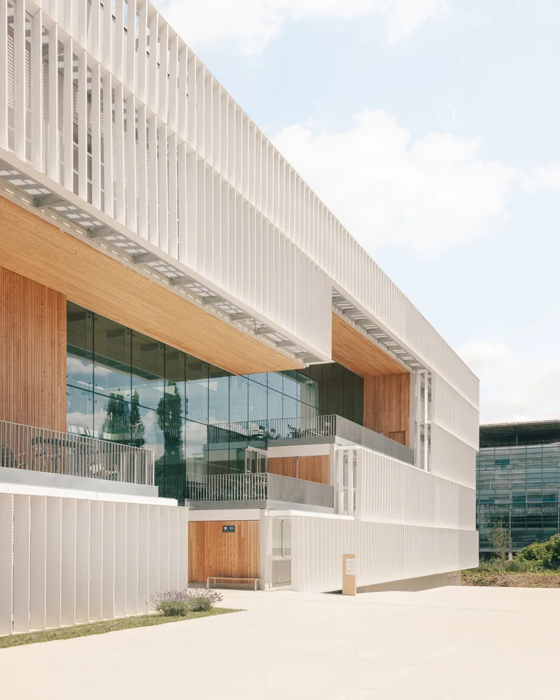 Side facade showing cantilevered timber-clad volumes with planted balconies beneath white vertical screens