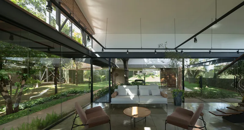 Open-plan living space beneath exposed steel structure with floor-to-ceiling glass overlooking garden courtyard