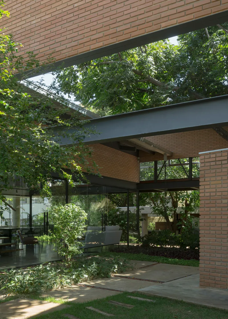 View through steel-framed canopy and glass walls into courtyard with preserved mature trees