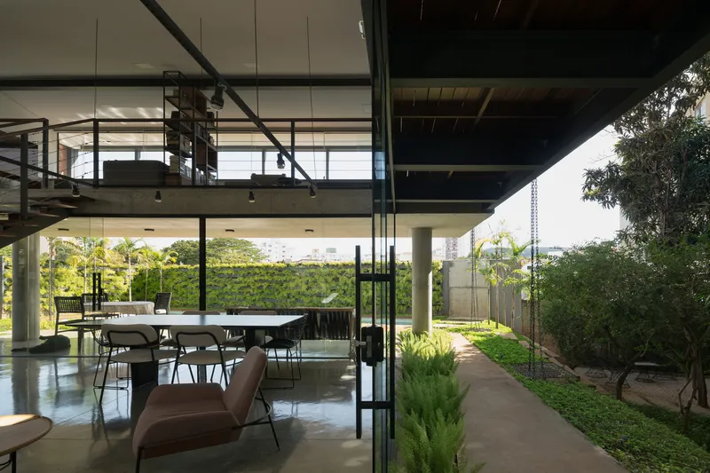 Interior dining area with mezzanine above opening onto landscaped pathway beside glass facade