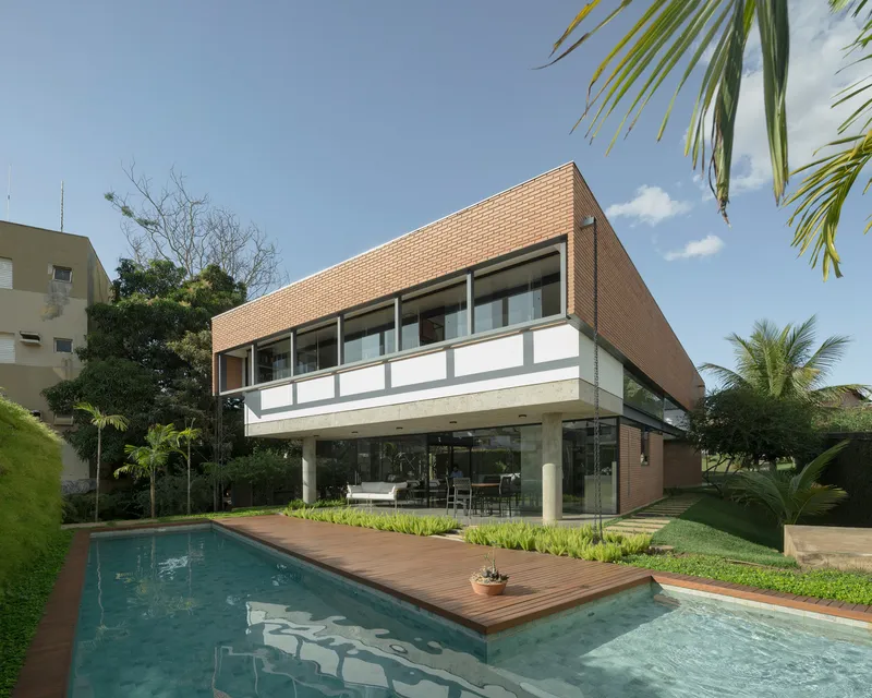 Two-story brick facade with cantilevered upper volume above pool and timber deck under palm trees