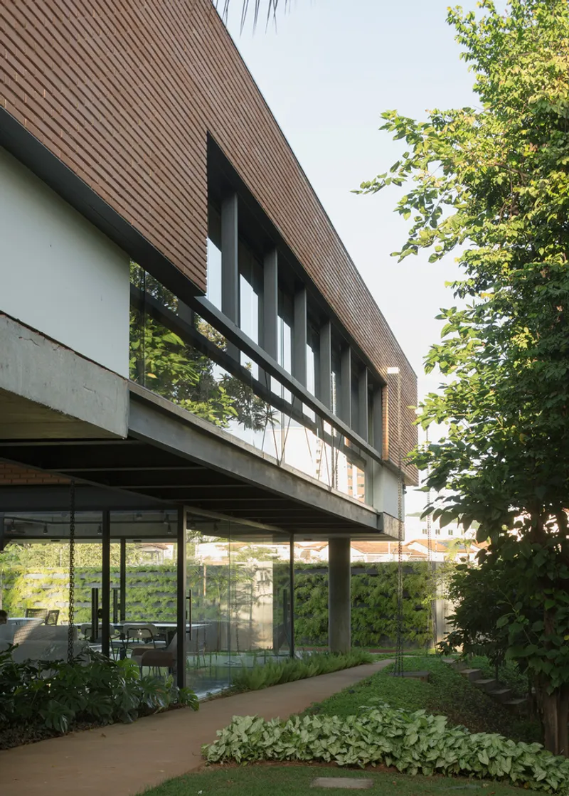 Street view of the elevated brick volume on concrete pillars with planted beds below