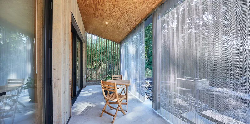 Covered porch with plywood ceiling and translucent corrugated screens filtering daylight onto concrete floor