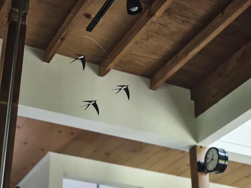 Exposed timber ceiling beams with suspended bird mobiles and wall-mounted clock in soft light