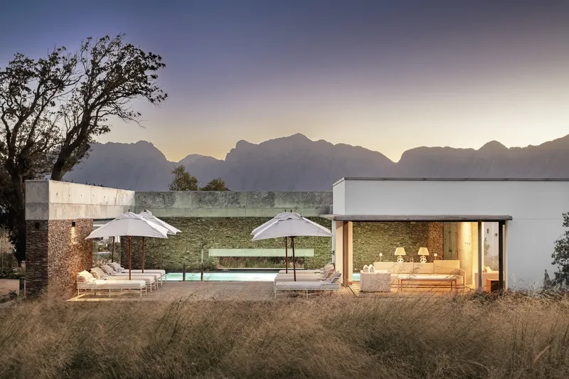 Terrace with pool and white umbrellas facing mountain range at sunset