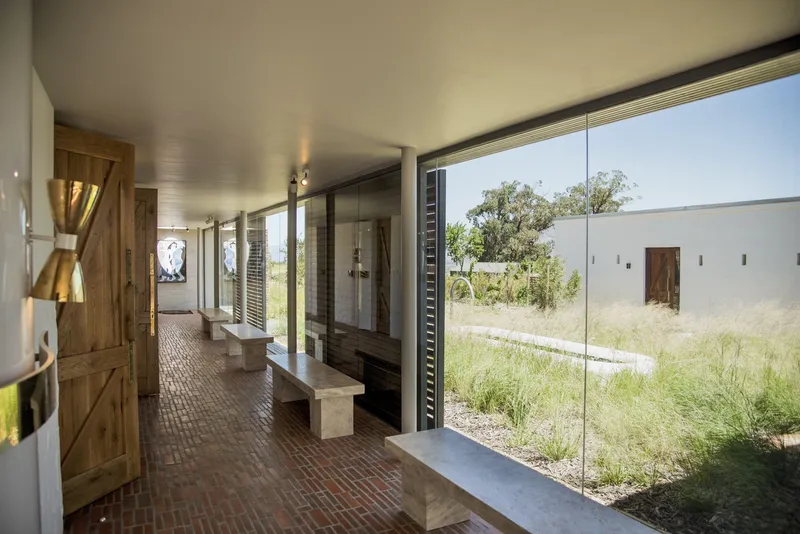 Interior corridor with brick paving and timber benches opening through glazed doors to a planted courtyard