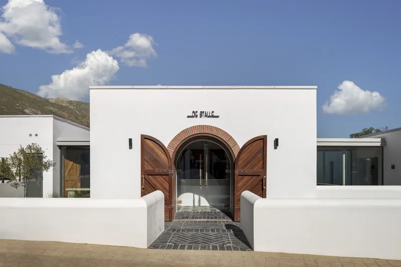White facade with arched timber doors and brick paving beneath scattered clouds
