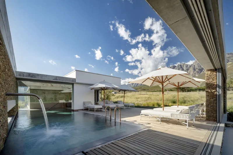 Covered terrace overlooking a pool with mountain views and white umbrellas on timber decking
