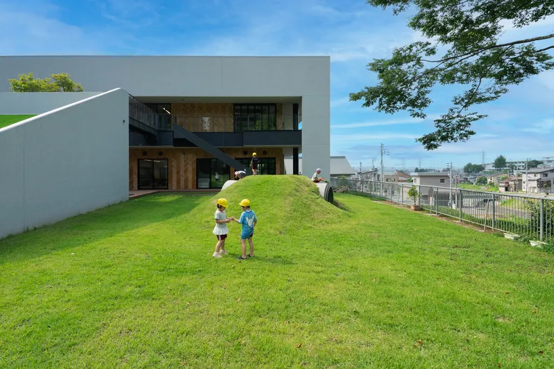 Sloped lawn with two children ascending toward the grey concrete facade and timber-clad recesses