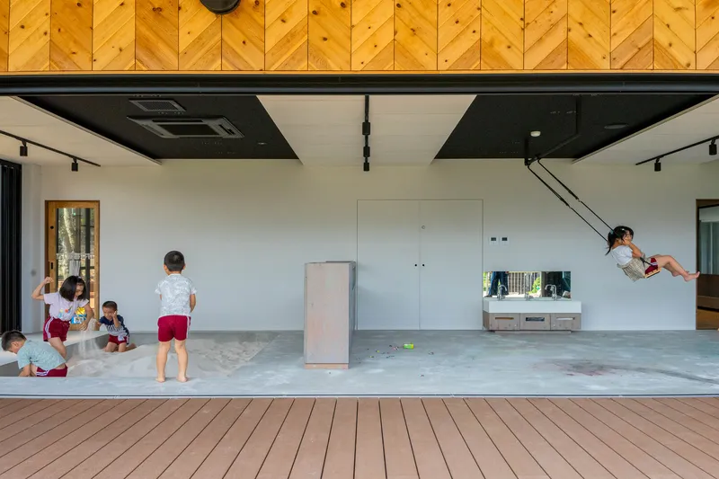 Open interior space with diagonal timber ceiling panels and children playing as one swings on a rope