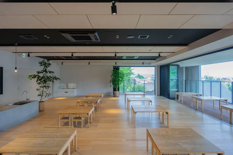 Interior classroom with rows of light timber tables and benches beneath black and beige ceiling panels