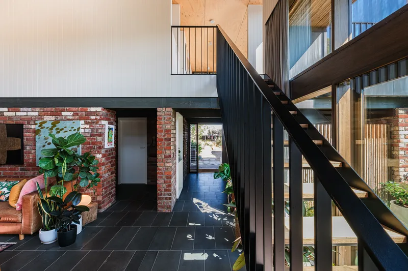 Double-height entry hall with black steel staircase, exposed brick walls and potted plants on dark tile floor