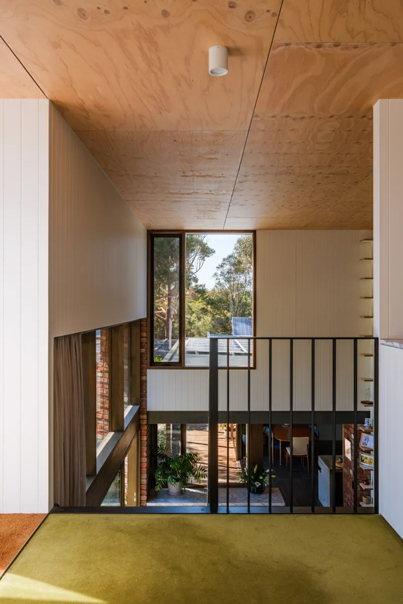 Upper floor landing with plywood ceiling, steel balustrade and corner window framing distant trees