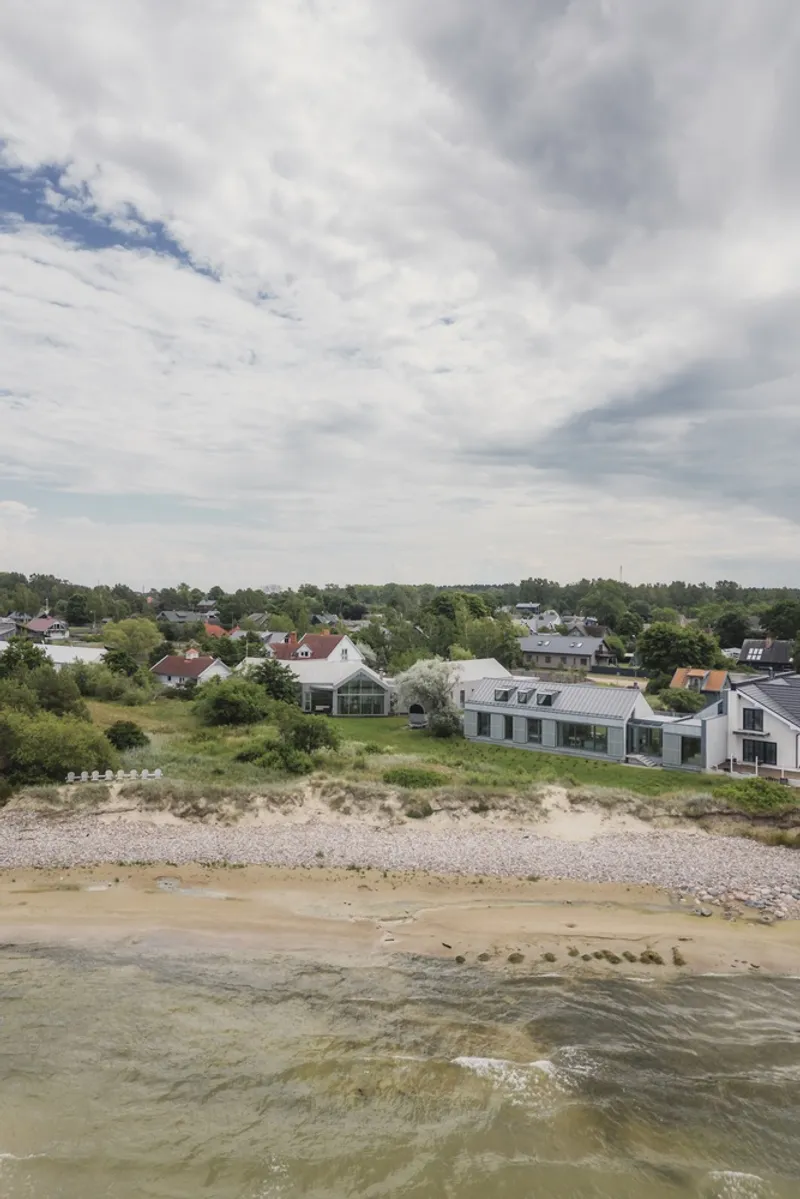 Aerial view of the metal-roofed residence along a pebble beach with neighboring houses inland