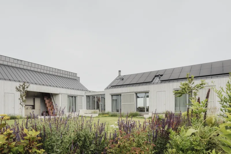 Courtyard view framed by flowering perennials showing two linked volumes with solar-paneled roofs