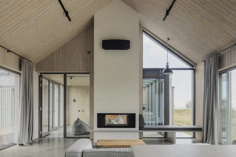 Living room with freestanding white fireplace core, timber-lined vaulted ceiling and full-height glass doors