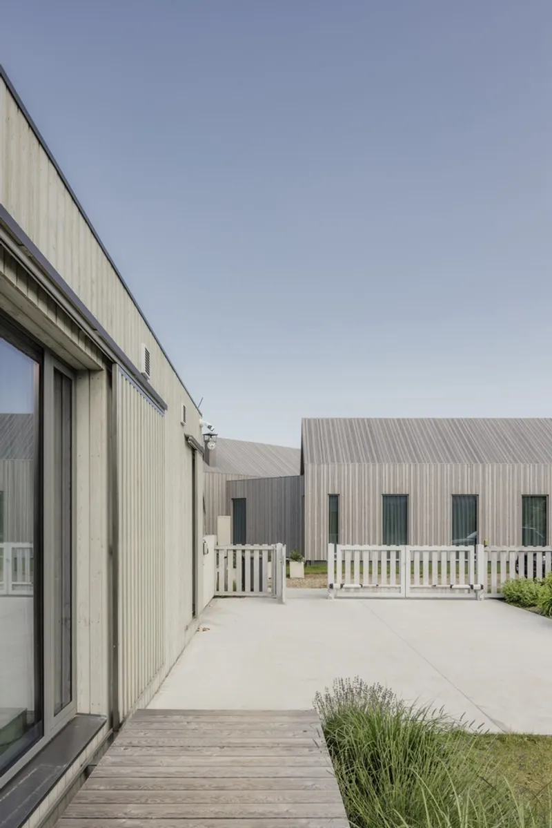 View across timber deck to corrugated metal facade and white painted fence enclosing paved courtyard