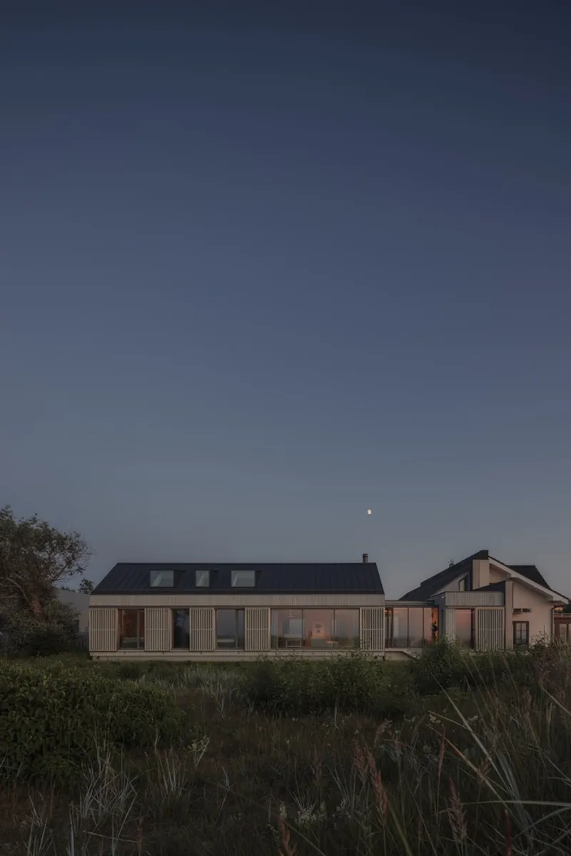 Facade of the timber-clad residence with vertical shutters and skylights at dusk with moon overhead