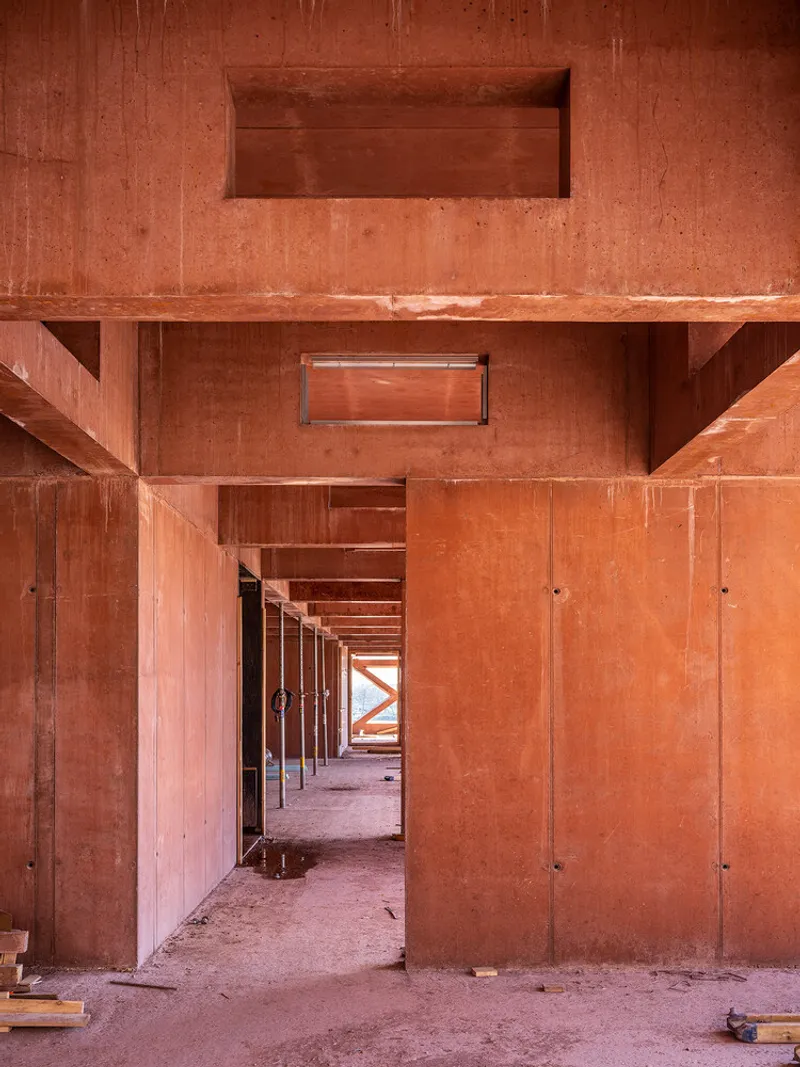 Interior corridor with exposed red concrete beams, columns and formwork marks during construction