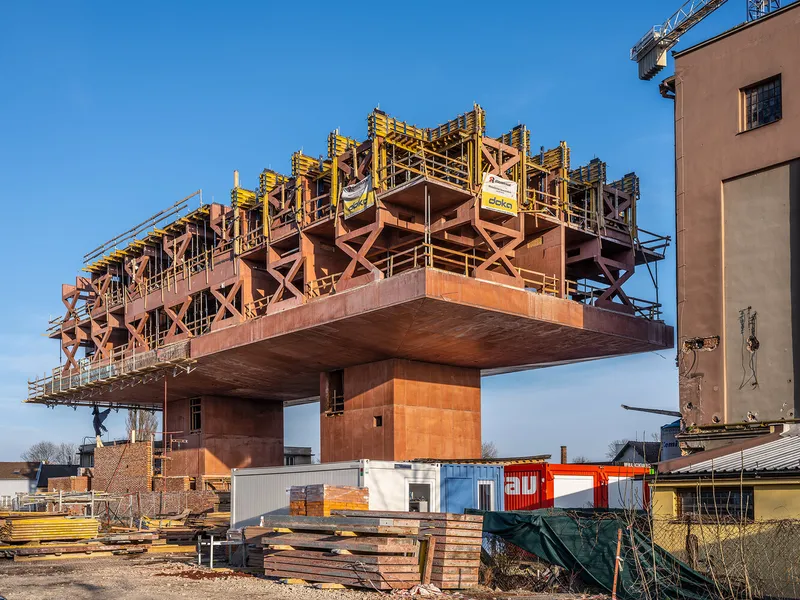 Elevated steel structure with exposed cross-bracing and formwork under a clear blue sky on an active construction site