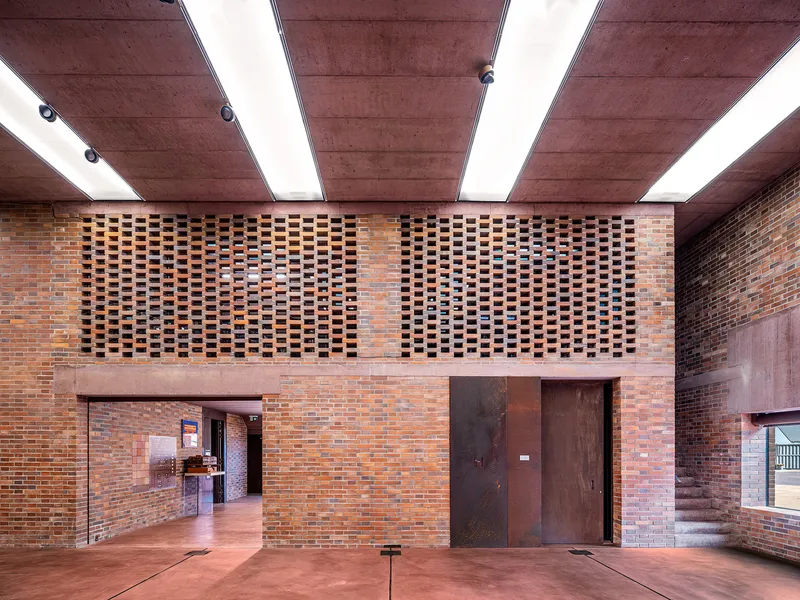Interior hall with perforated brick screen wall above weathered steel doors under a coffered concrete ceiling