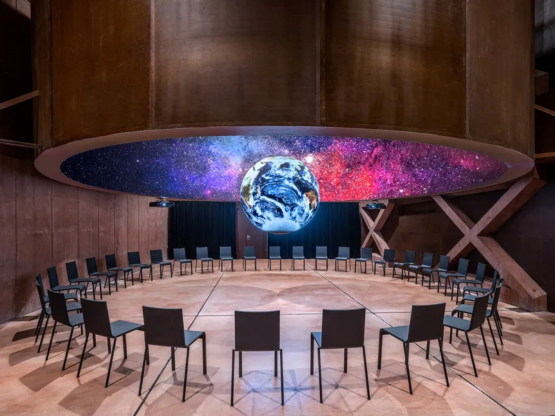 Circular seating arrangement below an illuminated earth globe and curved projection screen displaying a cosmic nebula