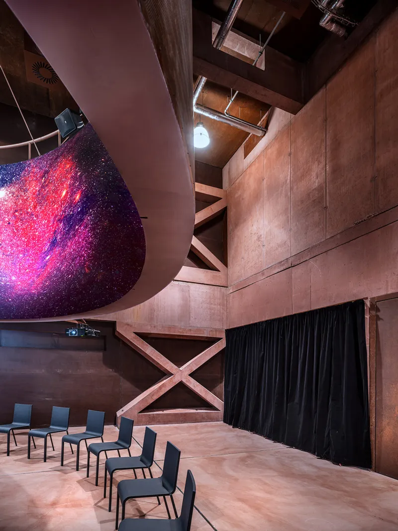 Upward view of the curved projection screen edge and exposed concrete bracing beside a row of chairs