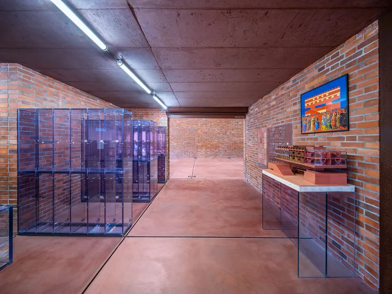 Gallery corridor with red brick walls, glass display cases, fluorescent ceiling lights, and terracotta flooring