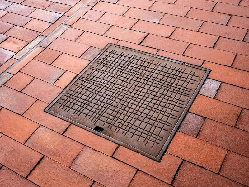 Metal drainage grate set into herringbone-patterned red brick paving