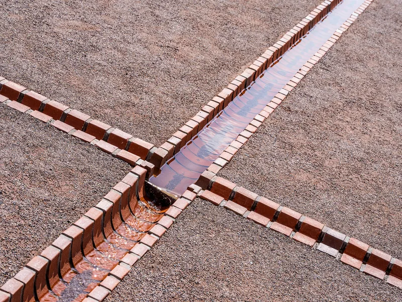 Red brick water channel crossing in X-pattern over gravel with shallow water flowing