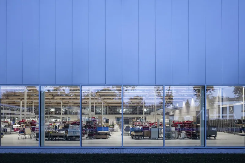 Blue metal panel facade with horizontal ribbon window exposing the double-height interior at dusk
