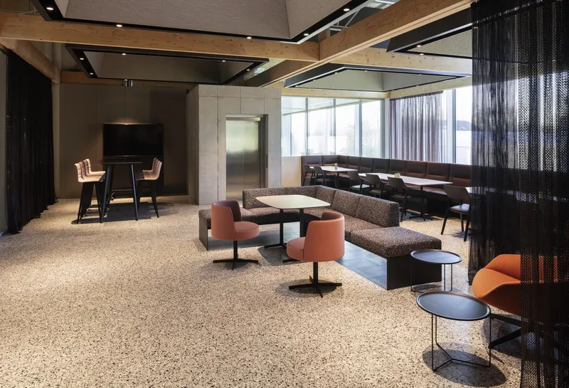 Lounge area with terrazzo flooring, metal mesh screens and salmon upholstered seating beneath timber ceiling