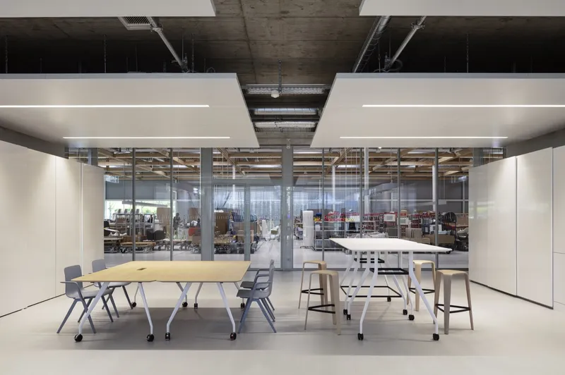 Meeting area with mobile tables and glazed partitions looking into the workshop beyond