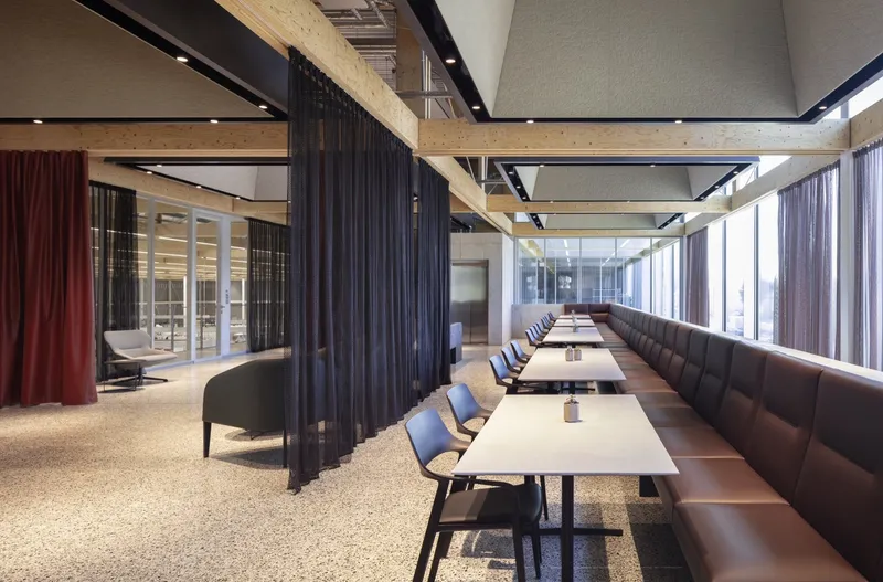 Cafeteria with banquette seating and timber beams separating dining zones with mesh and fabric curtains