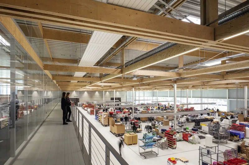 Upper level circulation corridor with glass railing where two figures overlook the warehouse below
